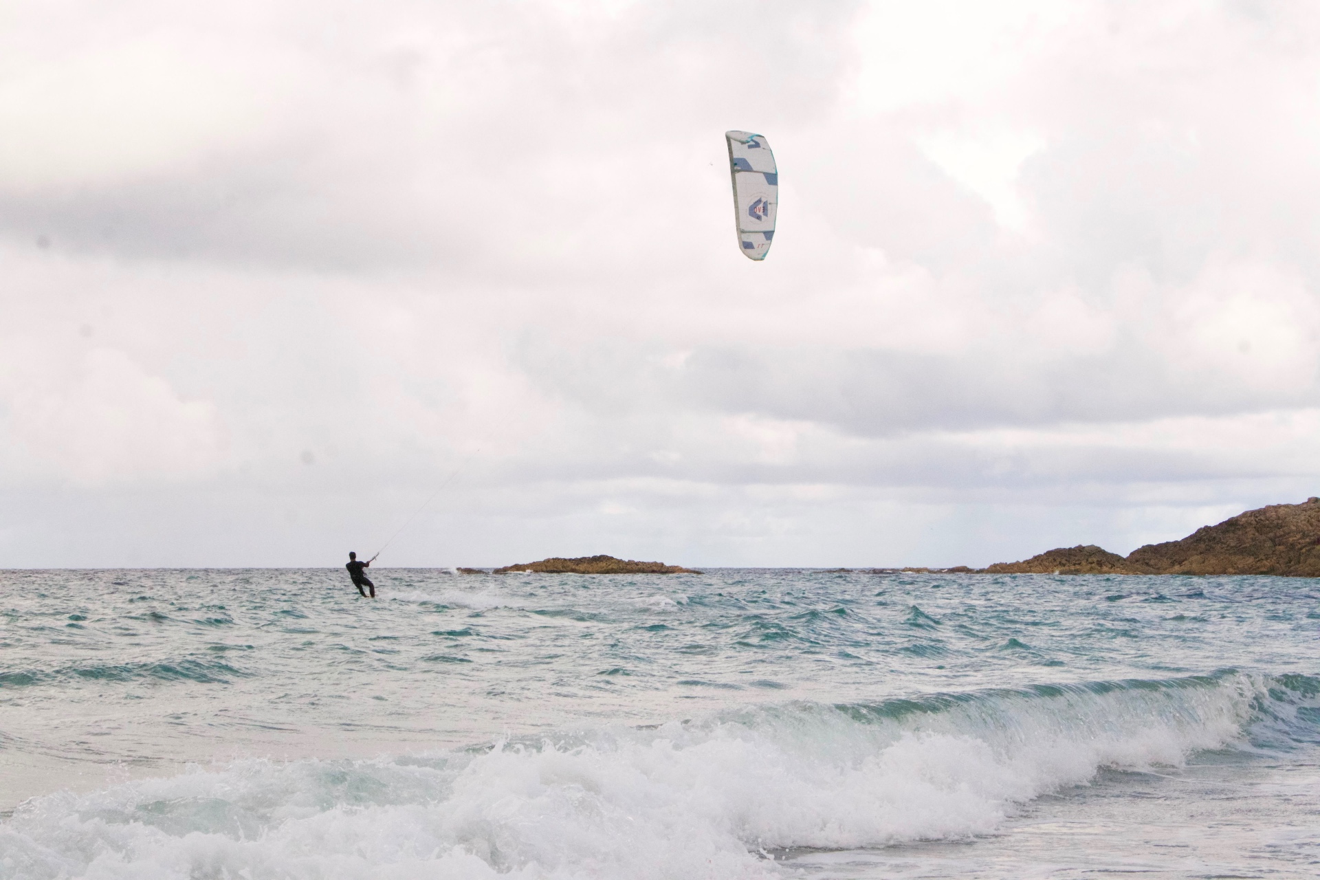 Kitesurfer riding a wind-blown swell off a rocky Scottish coastline