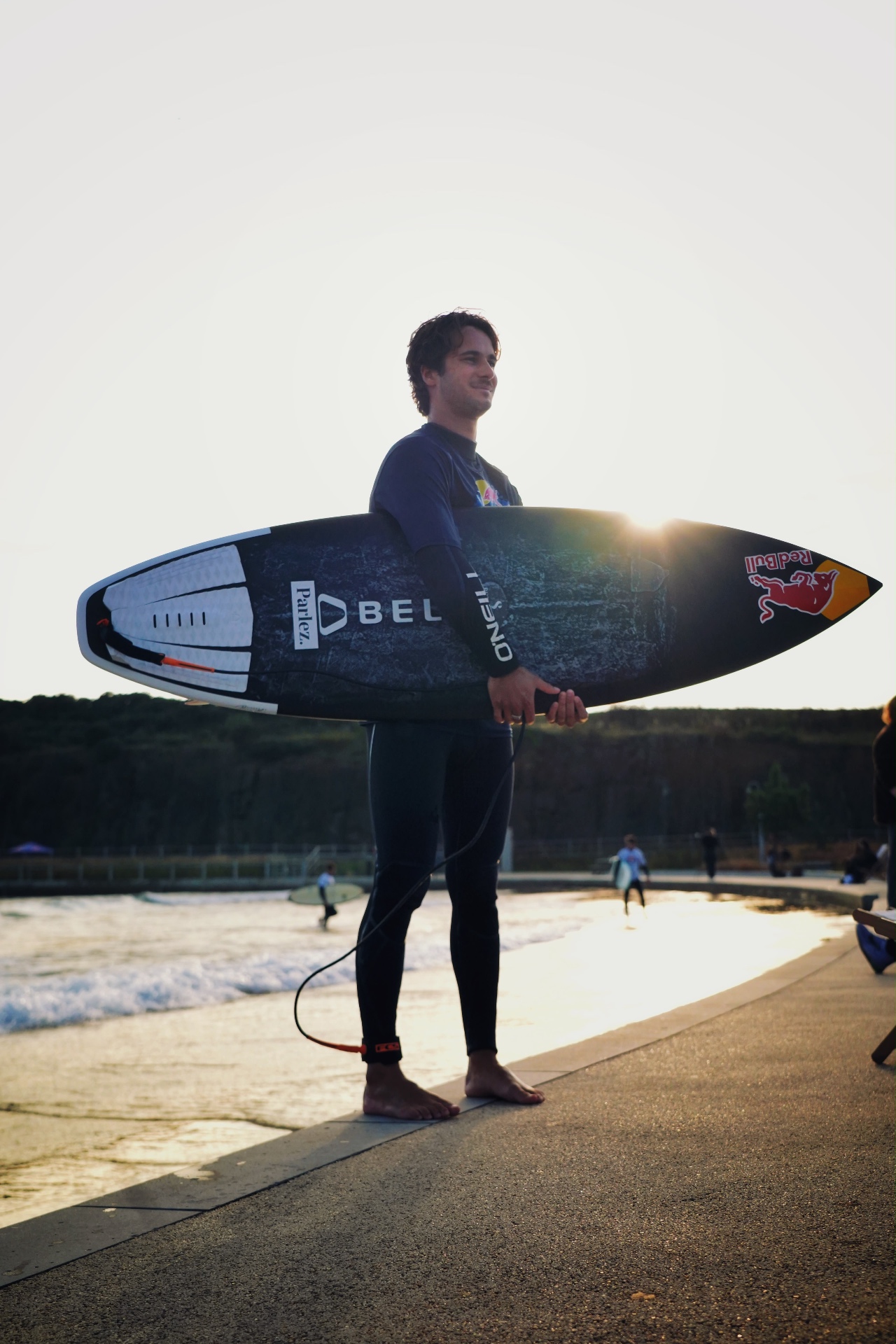 Surfer standing with his board at the water's edge in golden evening light