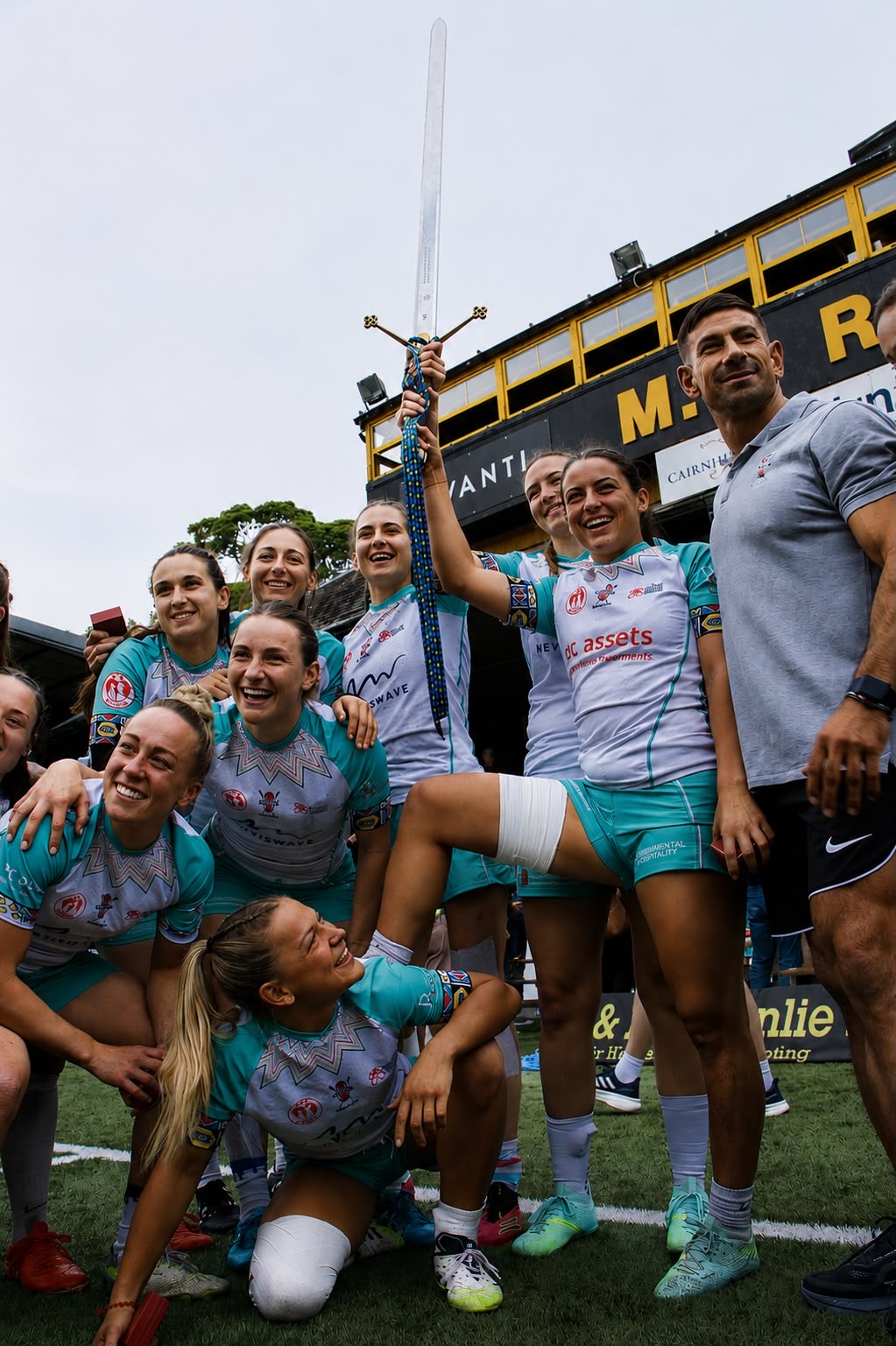 Women's sevens players posing triumphantly with the sword raised high