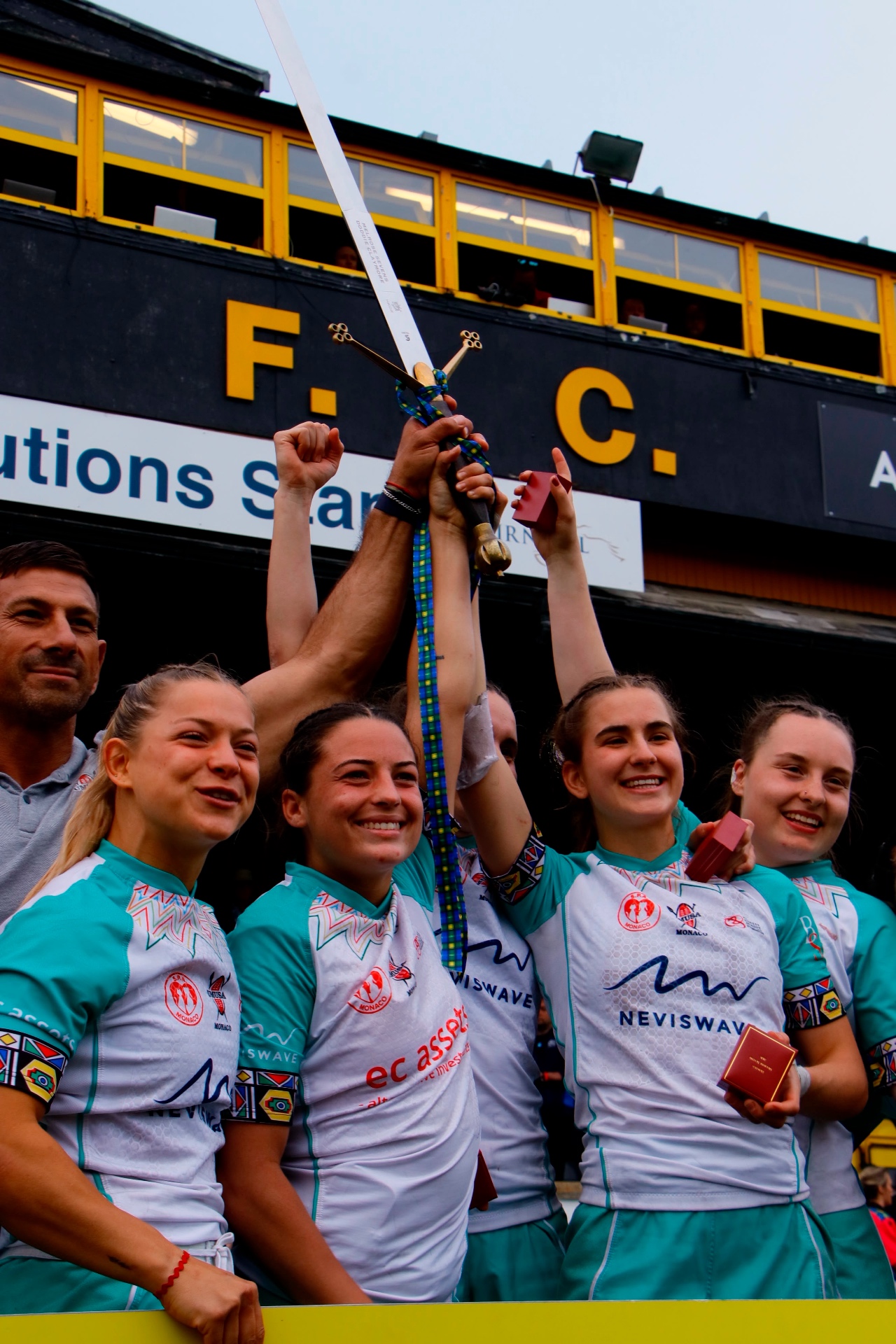 Sevens players lifting the ceremonial sword in front of the stand