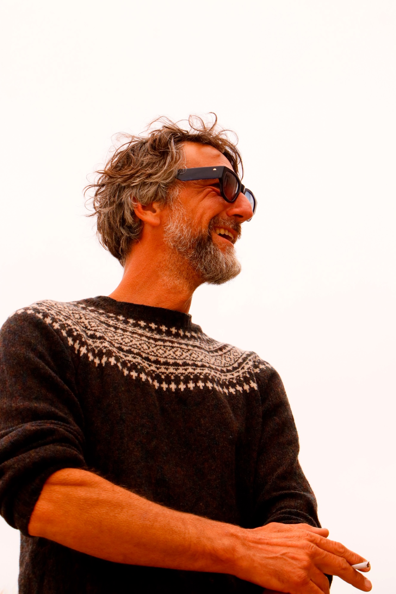 Portrait of a man laughing in a patterned wool jumper against a bright sky