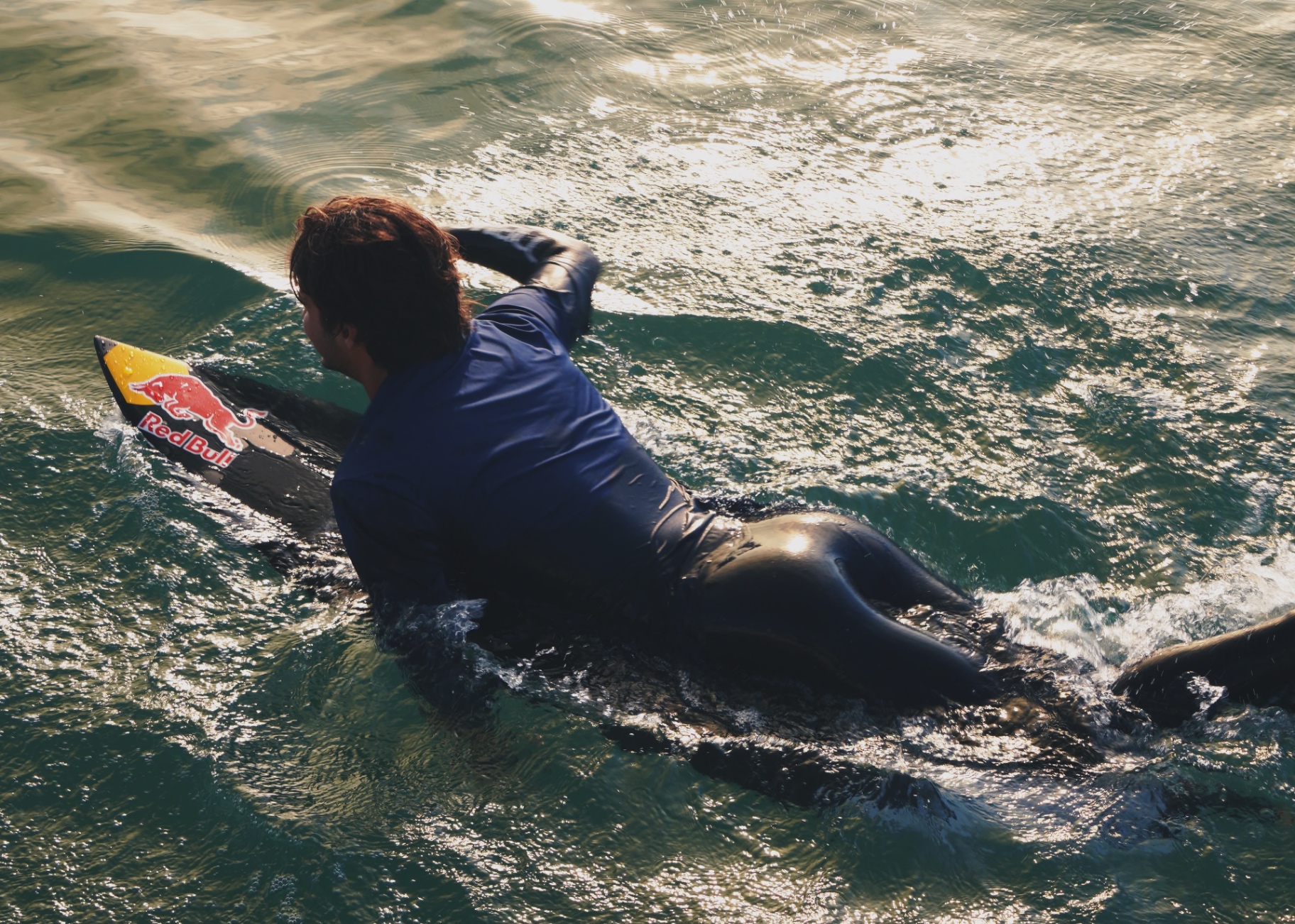Surfer paddling across golden evening water