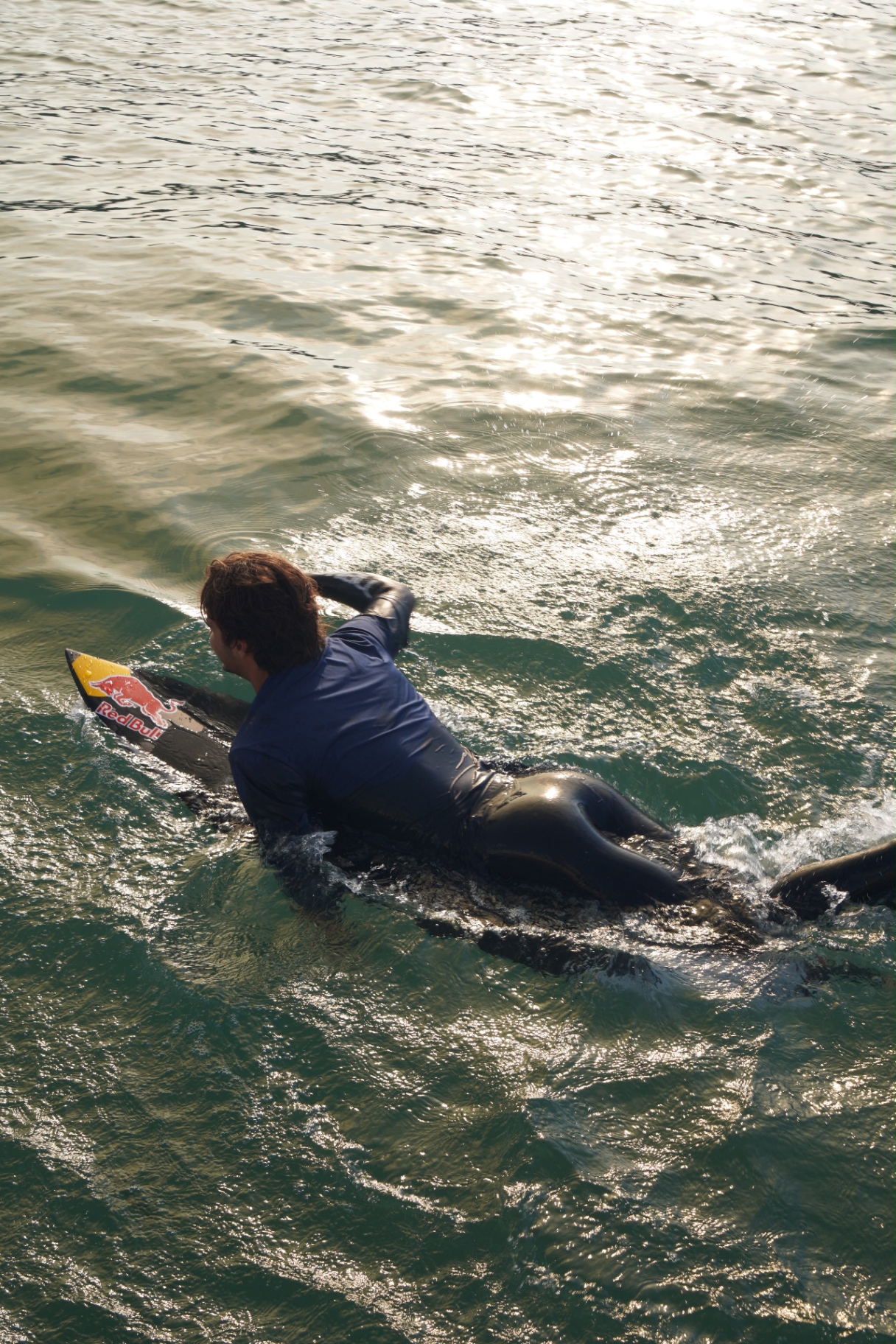 Surfer paddling out through glassy backlit water