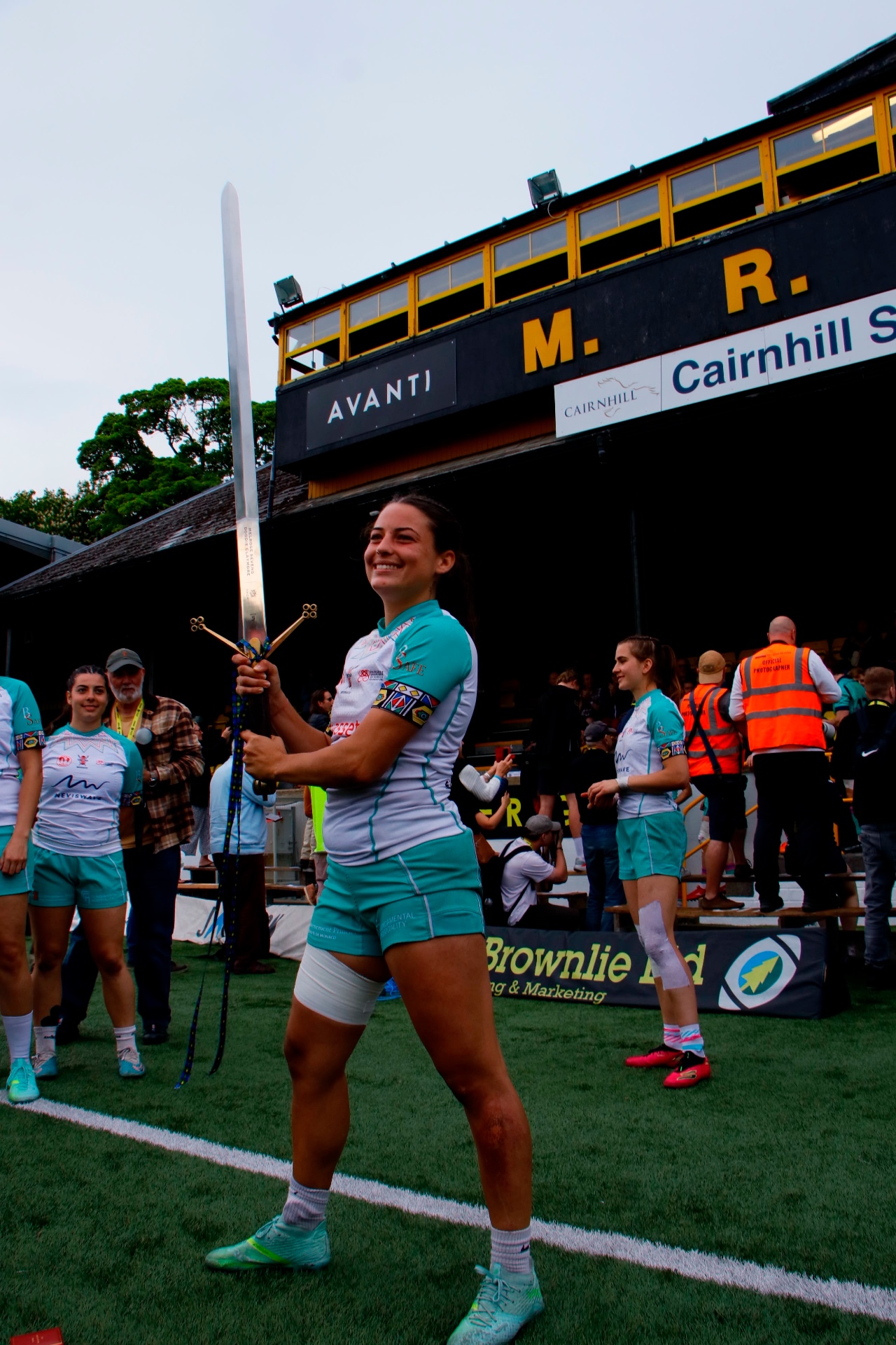 Sevens player smiling with the ceremonial sword on the rugby pitch