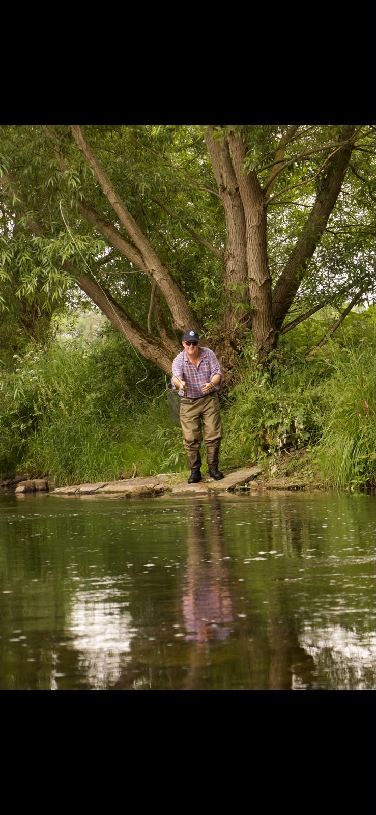 Fly fisherman on the riverbank beneath an overhanging willow