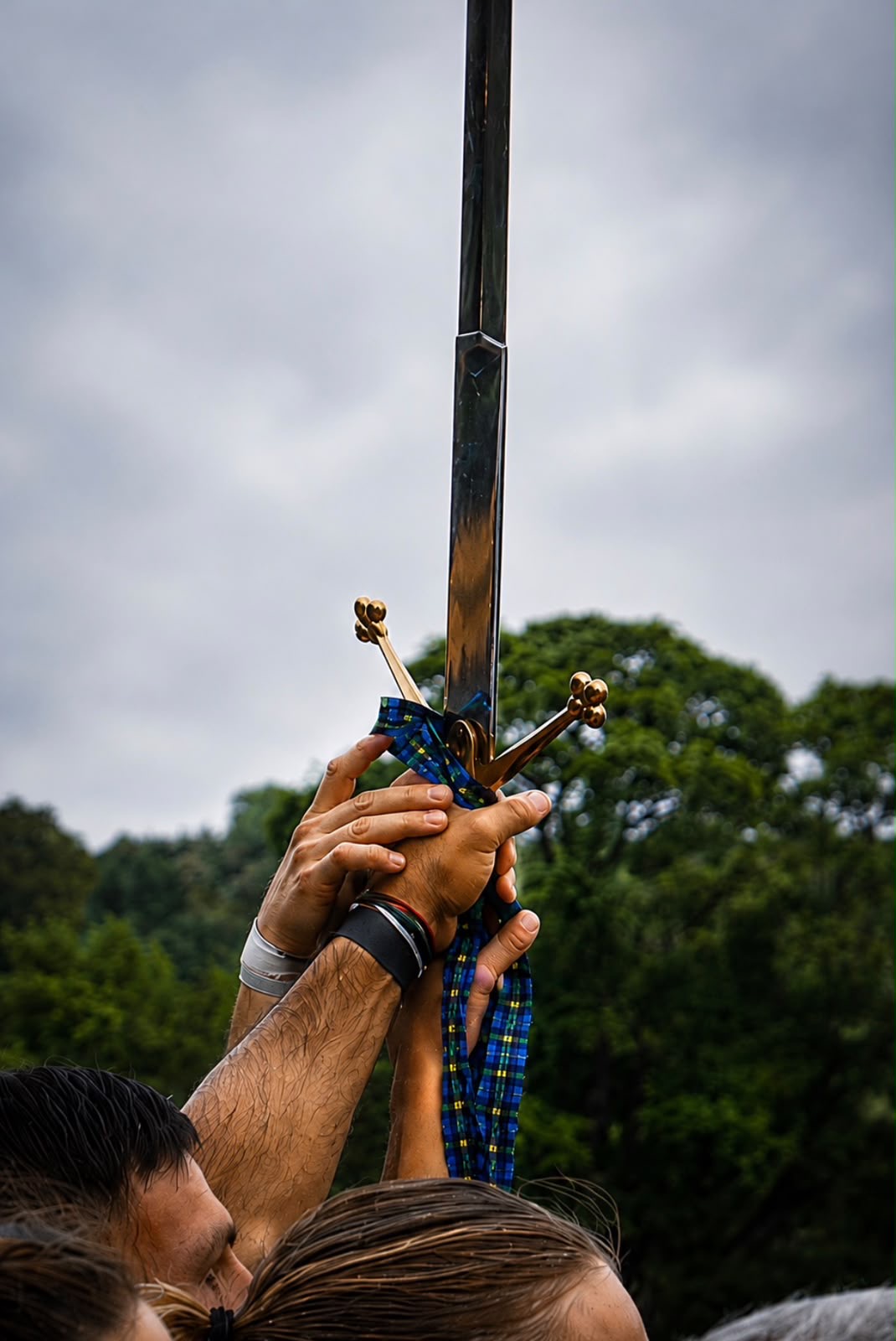 Hands lifting the ceremonial sword against a grey Borders sky