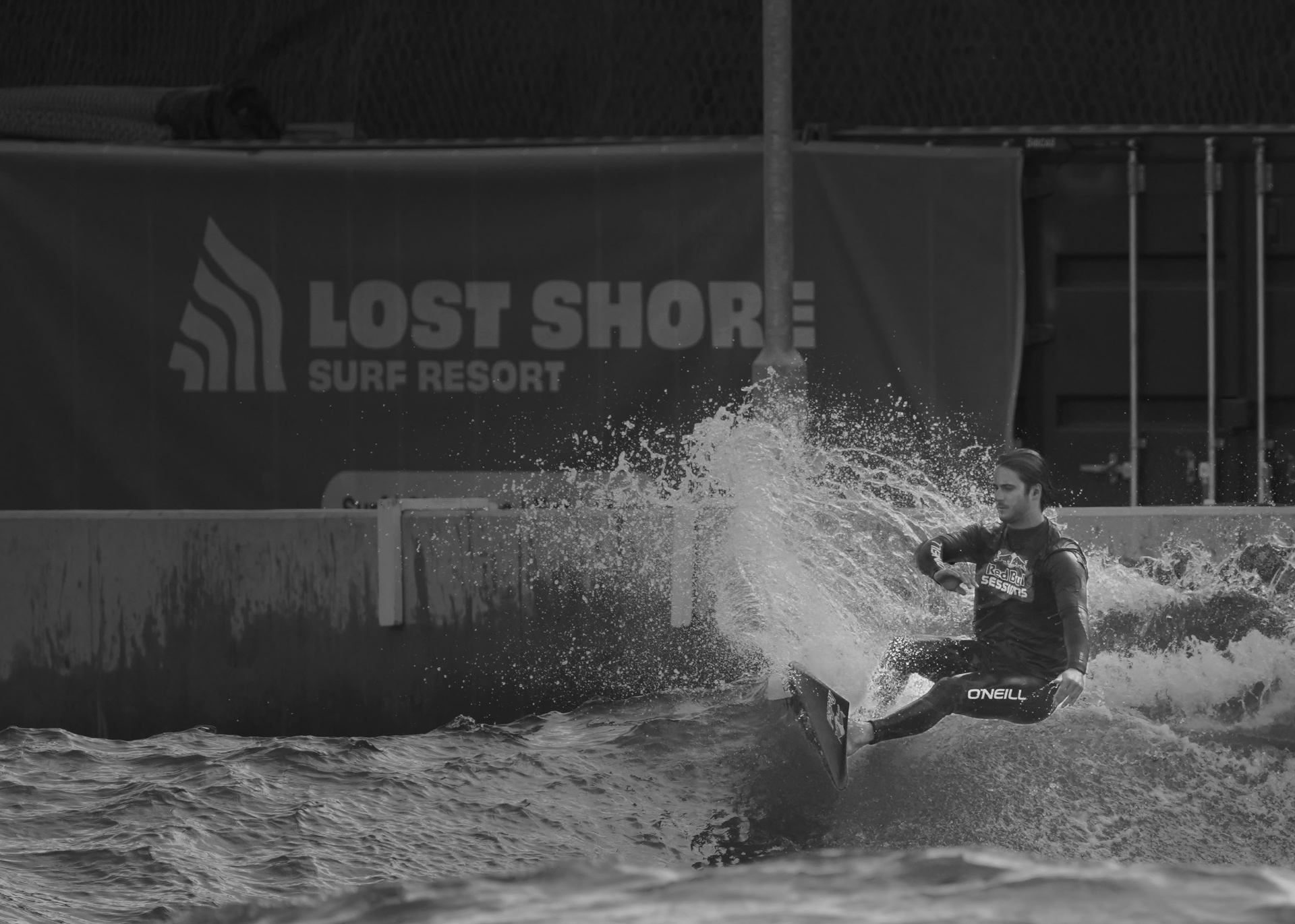 Black and white frame of a surfer carving in front of the Lost Shore banner