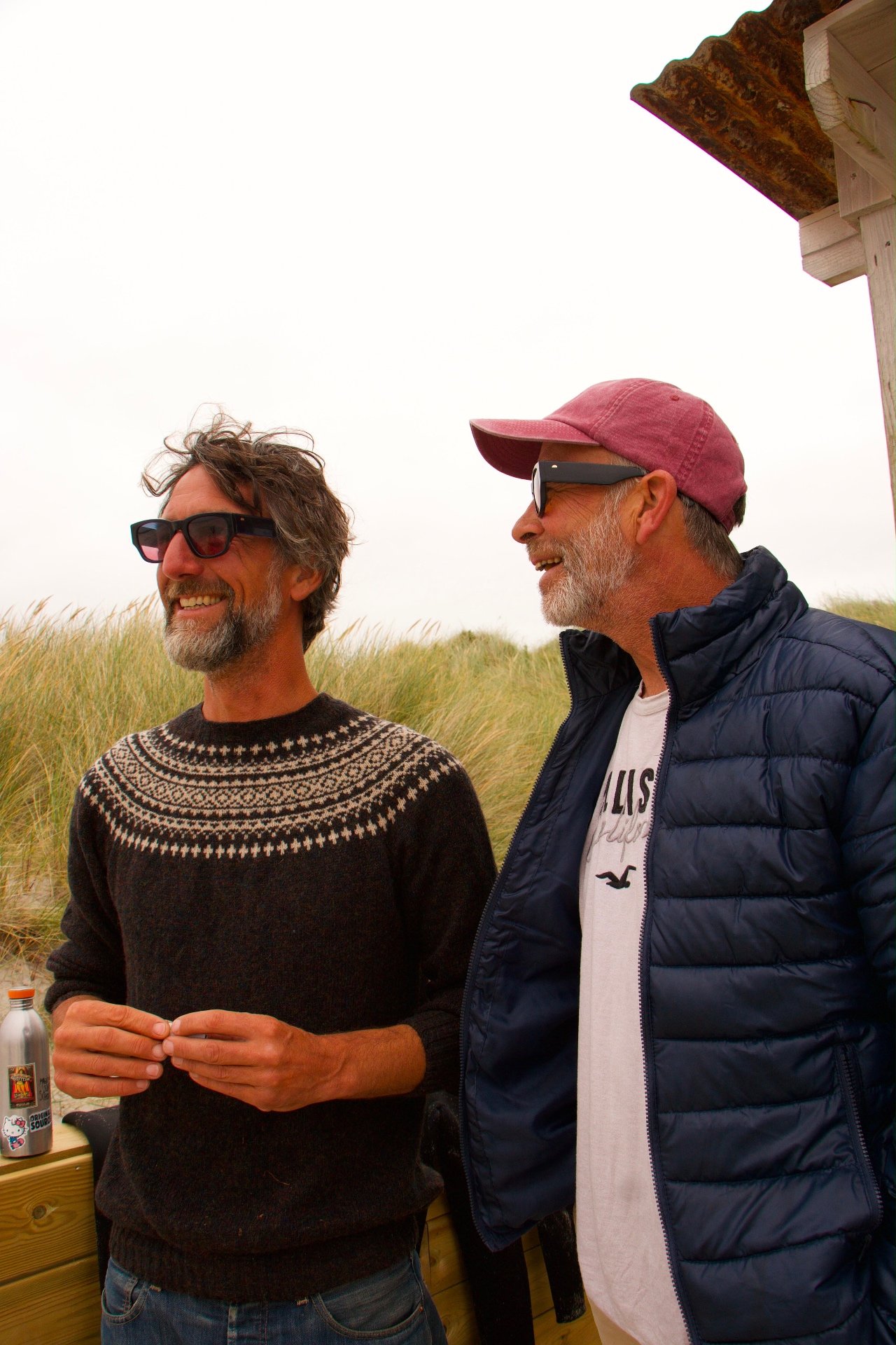 Two friends laughing beside a beach hut in the dunes