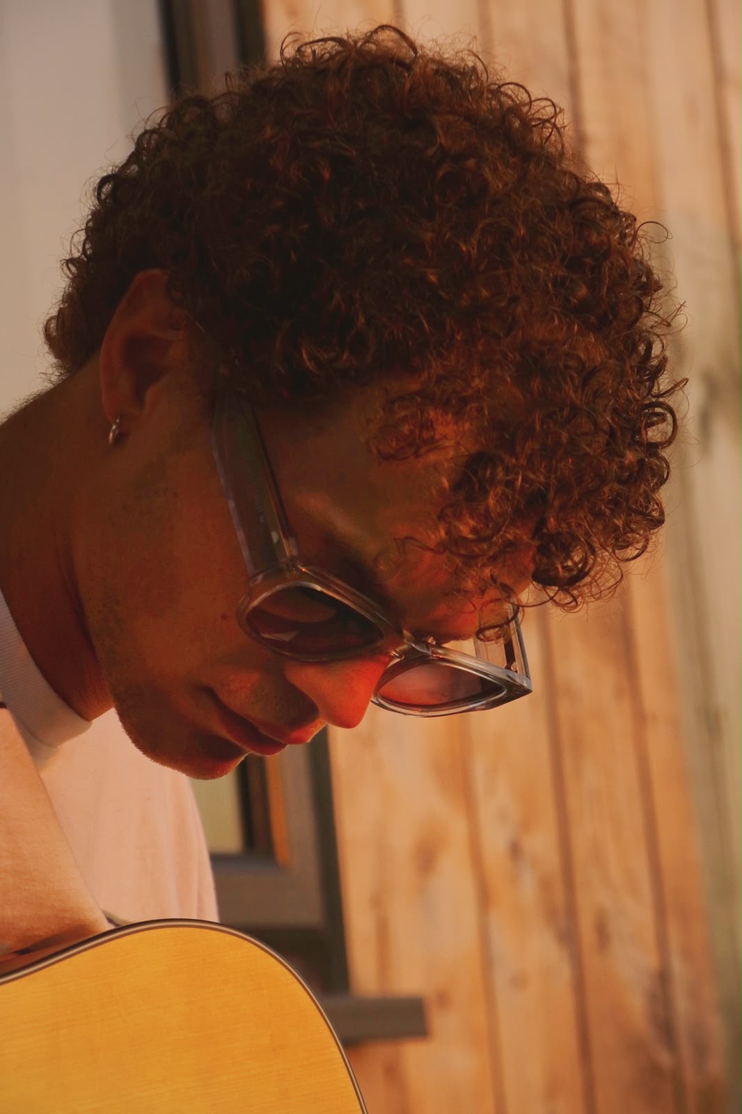 Close portrait of a guitarist in clear-framed TENS sunglasses at golden hour
